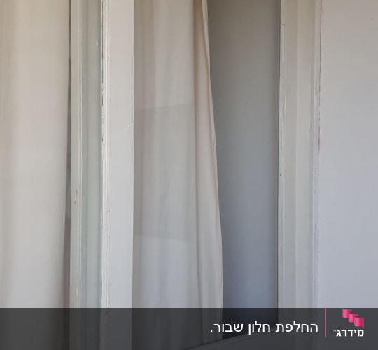 חלון זכוכית עם וילון לבן מאחוריו